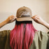Person wearing a cap with 'Faith' text and pink hair against a beige background